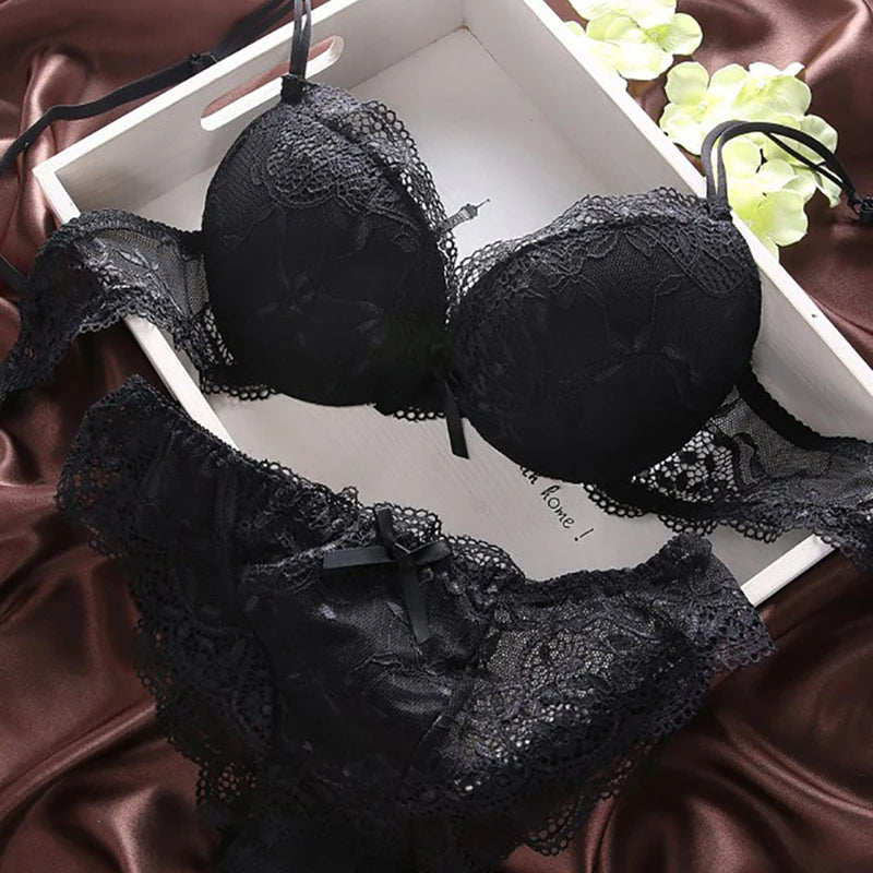 Black lace bra and panties set on a satin surface with grapes in the background