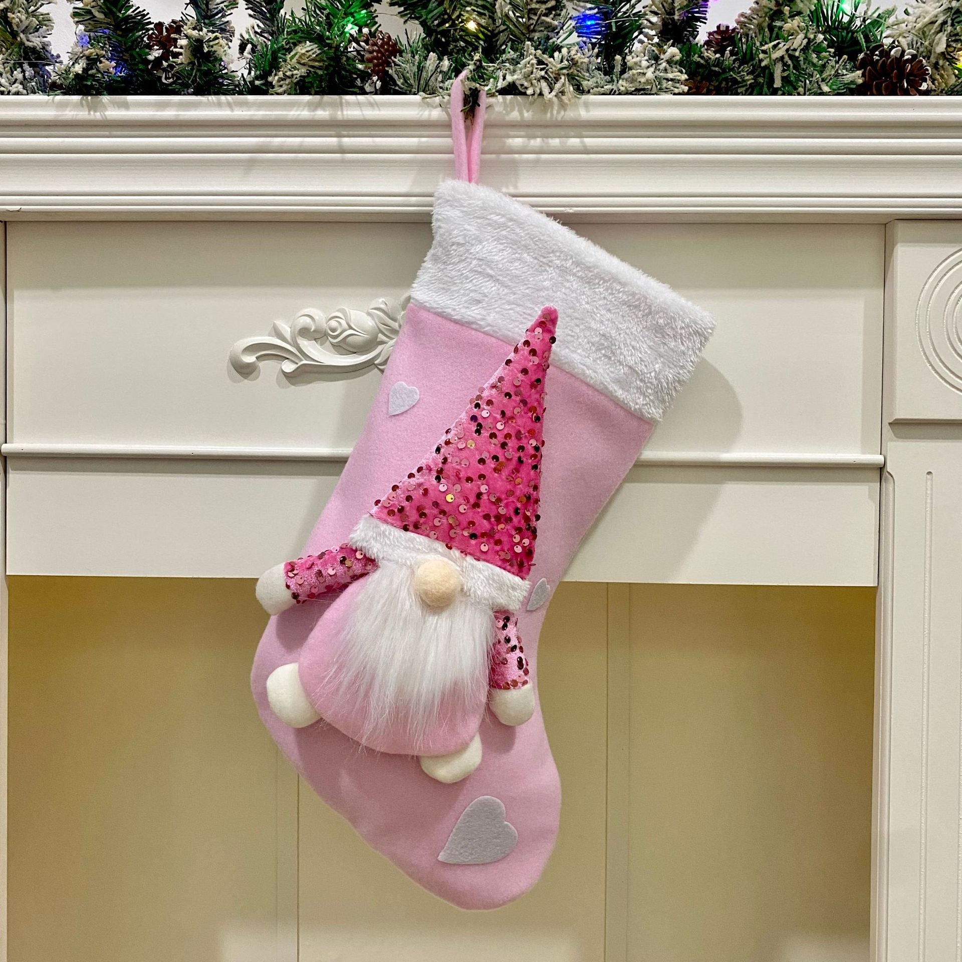Pink Christmas stocking with gnome design hanging on a fireplace mantle.